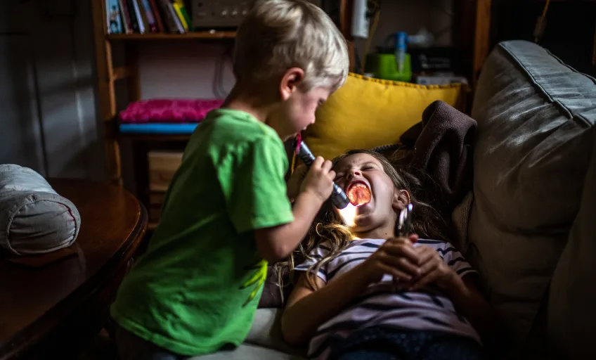 Allergies : un garçon éclaire la bouche ouverte d'une fillette avec une lampe de poche