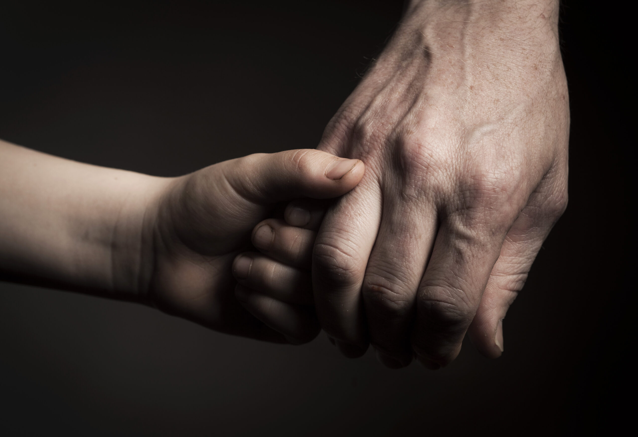 Cropped image of father and son holding hands against black background Adoptivkinder: Der Bruch in der Kindheit