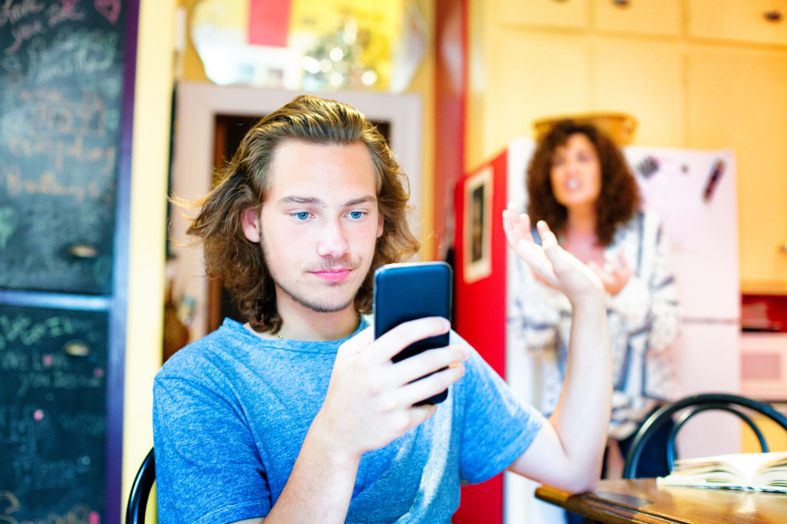 Male teenager ignoring scolding mom with mobile phone die Angst etwas am Smartphone zu verpassen