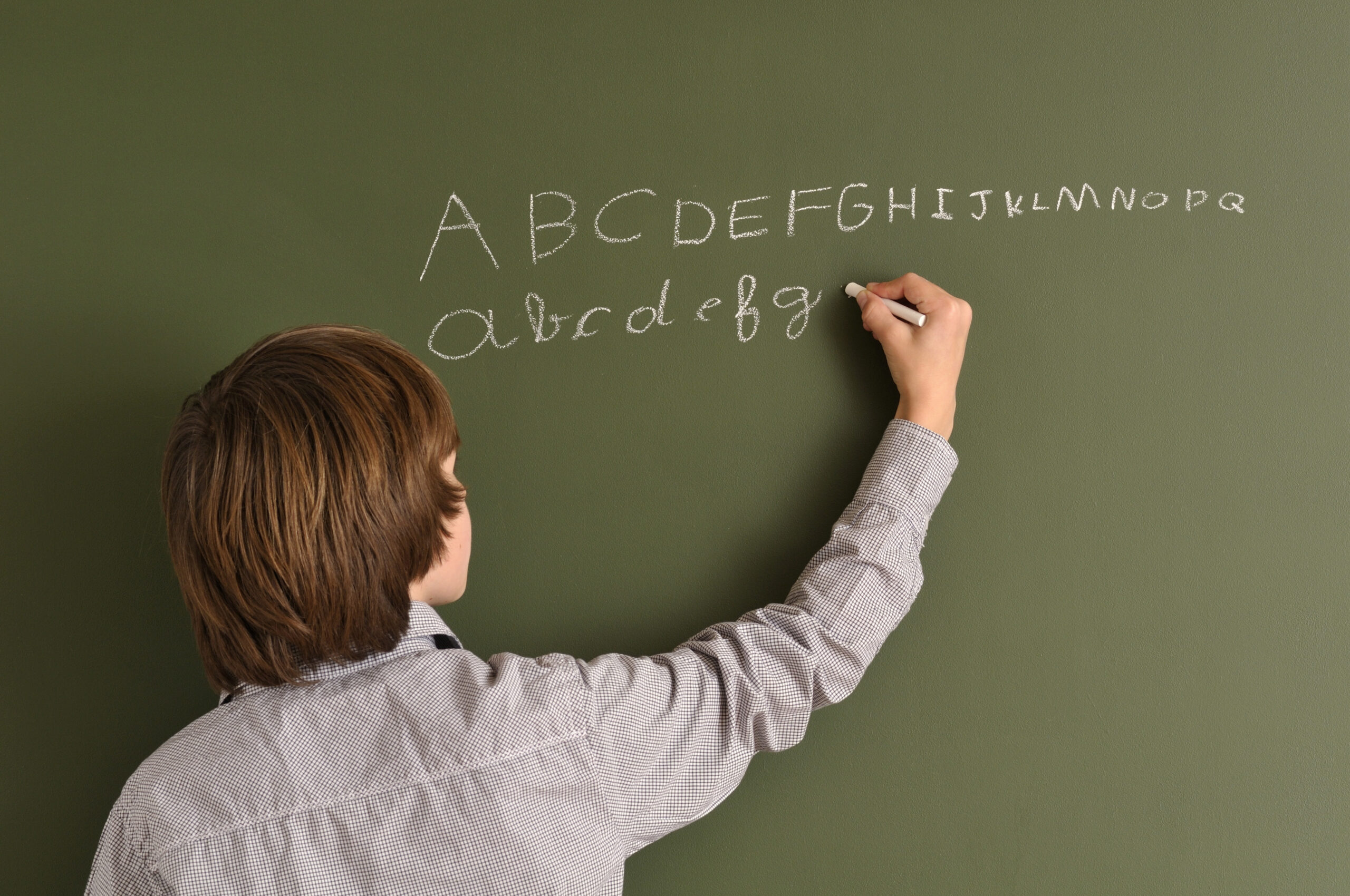Junge schreibt an eine Schultafel Kommt die Handschrift zu kurz?