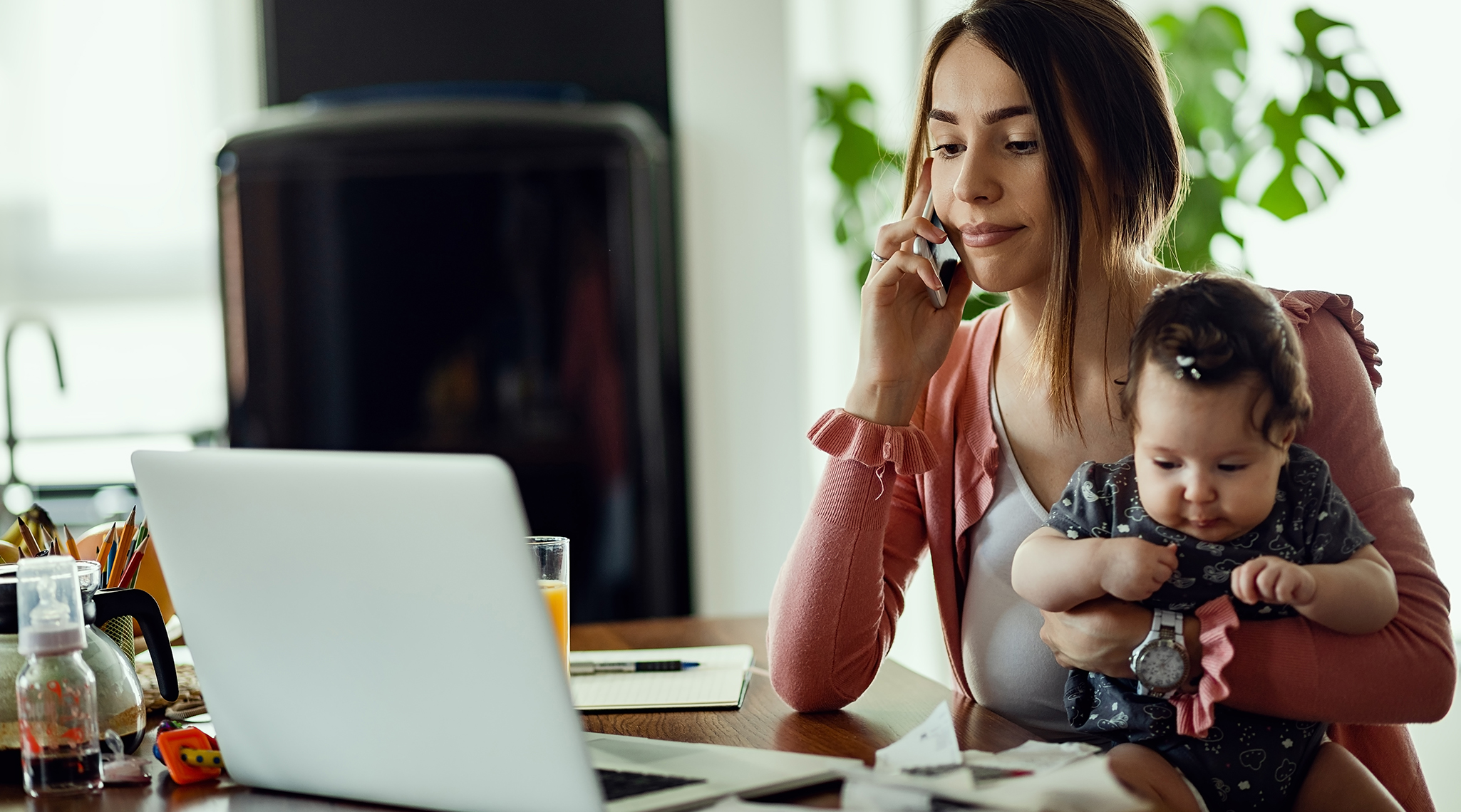 Young mother talking on the phone while using laptop at home.
