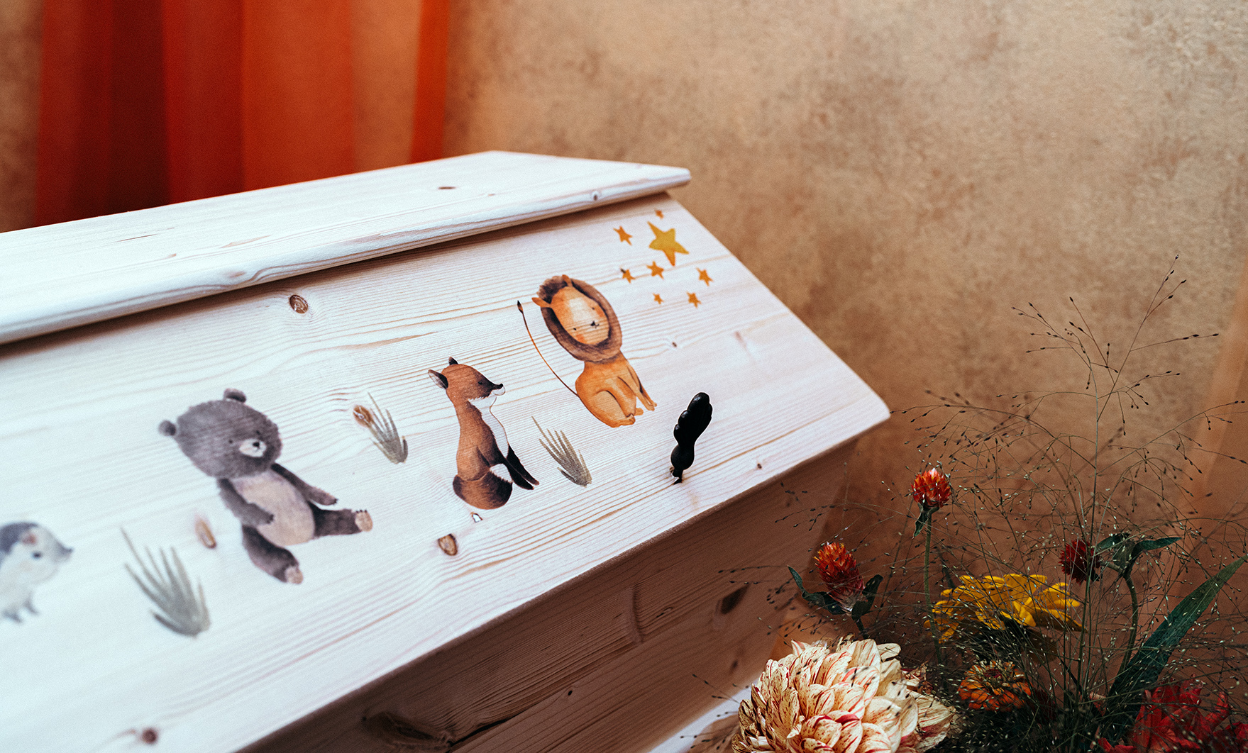 Wenn Kinder sterben – Wie Trauerfamilien halt finden können. Ein Kindersarg mit Tiersymbolen und Blumen im Trauerraum.