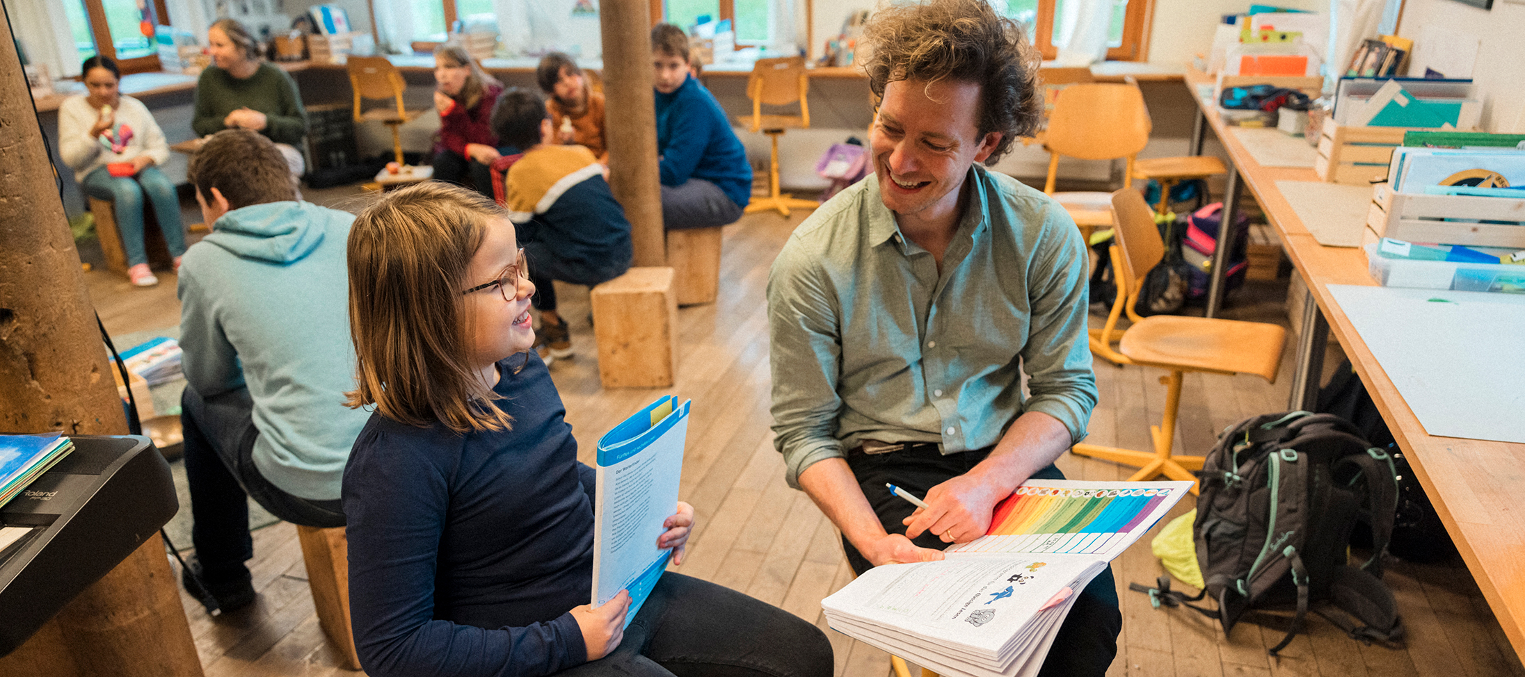 Alternativen zur Note. Lehrer sitzt im Klassenzimmer mit Kind und bespricht dessen Leistung.