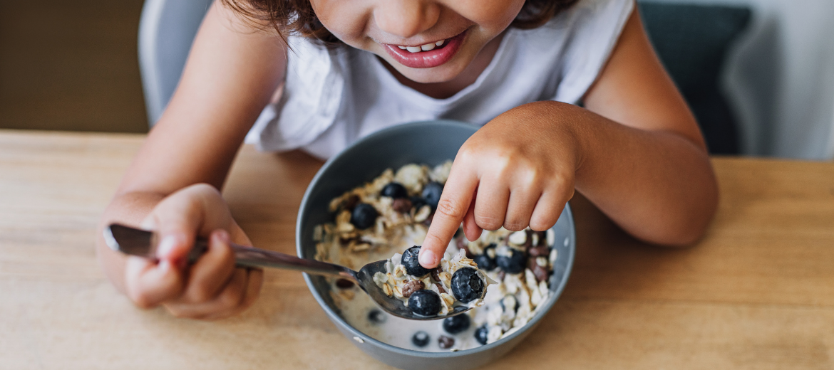 2024 Betty Bossi Vitamine Tipps richtiges Frühstück für Kinder und Jugendliche Wina Fontana Fritz und Fraenzihg Ein kleines Kind lacht während es am Tisch sein Frühstück einnimmt. Mehr Tipps für ein gesundes Frühstück gibt es im Artikel von Betty Bossi.