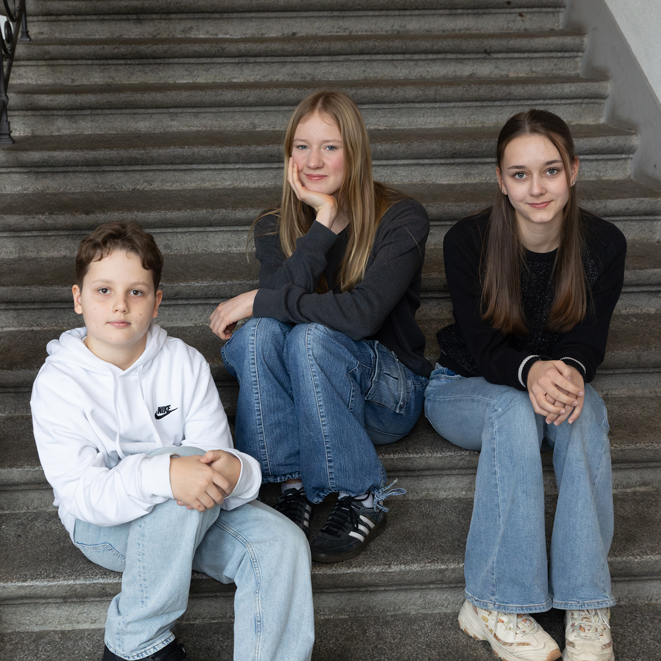 Drei Kinder sitzen auf einer Treppe in der Schule und sprechen über Social Media.