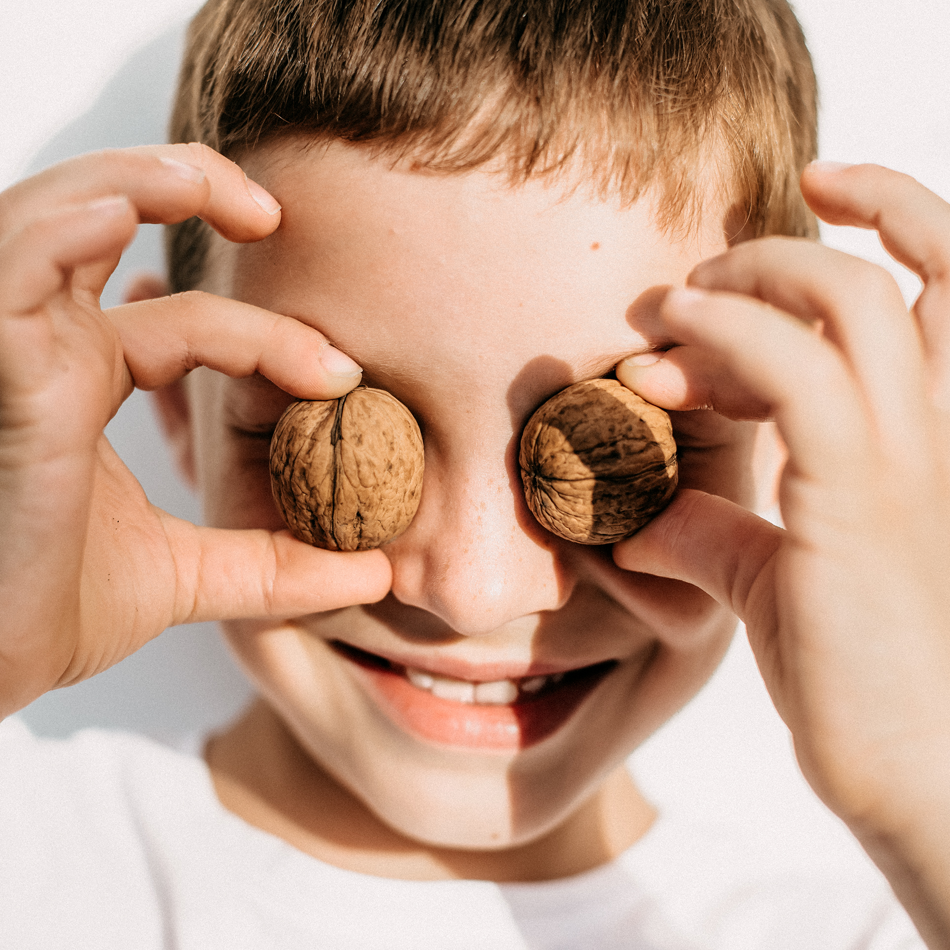 Gesunde Fette in der Ernährung. Ein Junge verdeckt sich mit Walnüssen die Augen.