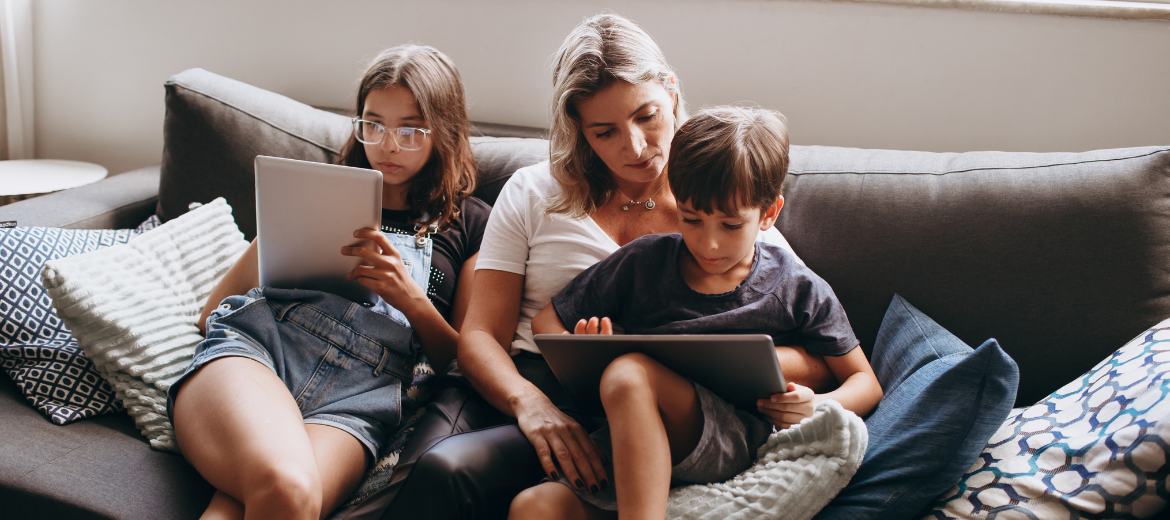 25-04-handy-regeln-swisscom-schweizer-elternmagazin-hg Regeln und Zuwendung: Mutter sitzt mit Tochter und Sohn auf dem Sofa. Beide Kinder schauen in ein Tablet.