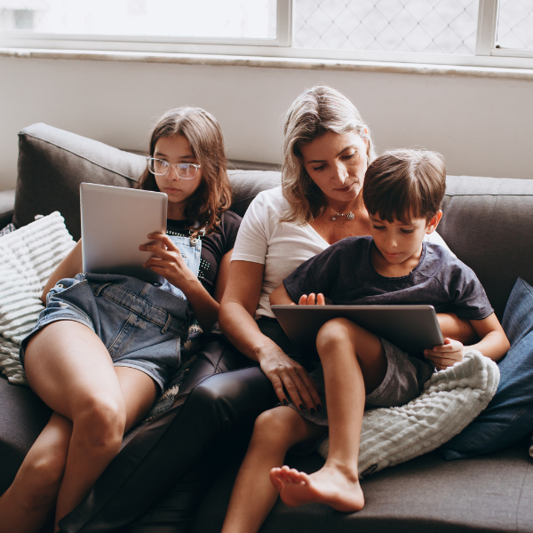 Regeln und Zuwendung: Mutter sitzt mit Tochter und Sohn auf dem Sofa. Beide Kinder schauen in ein Tablet.